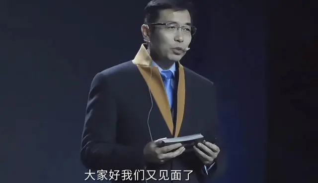 图片展示的是商汤科技年会上,以数字人技术“复活”的汤晓鸥的形象。他身着深色西装,佩戴金色领带,手持黑色物品,背景为深色。画面下方有白色字幕“大家好我们又见面了”。该图片与上下文紧密相关,上下文介绍了汤晓鸥数字人在年会上以数字化形象与参会者交流,惟妙惟肖且生动幽默,此图正是这一场景的呈现。