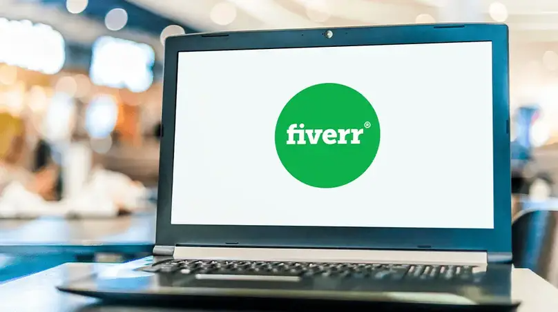 图片展示了一台笔记本电脑,屏幕上显示着Fiverr平台的标志,标志由一个绿色圆圈和白色“fiverr”字样组成。背景模糊,隐约可见室内环境。该图片与文档中介绍Fiverr平台的内容相关,直观呈现了Fiverr的标志,辅助说明Fiverr作为国际化的众包平台,为全球用户提供多种多样的服务这一背景信息。