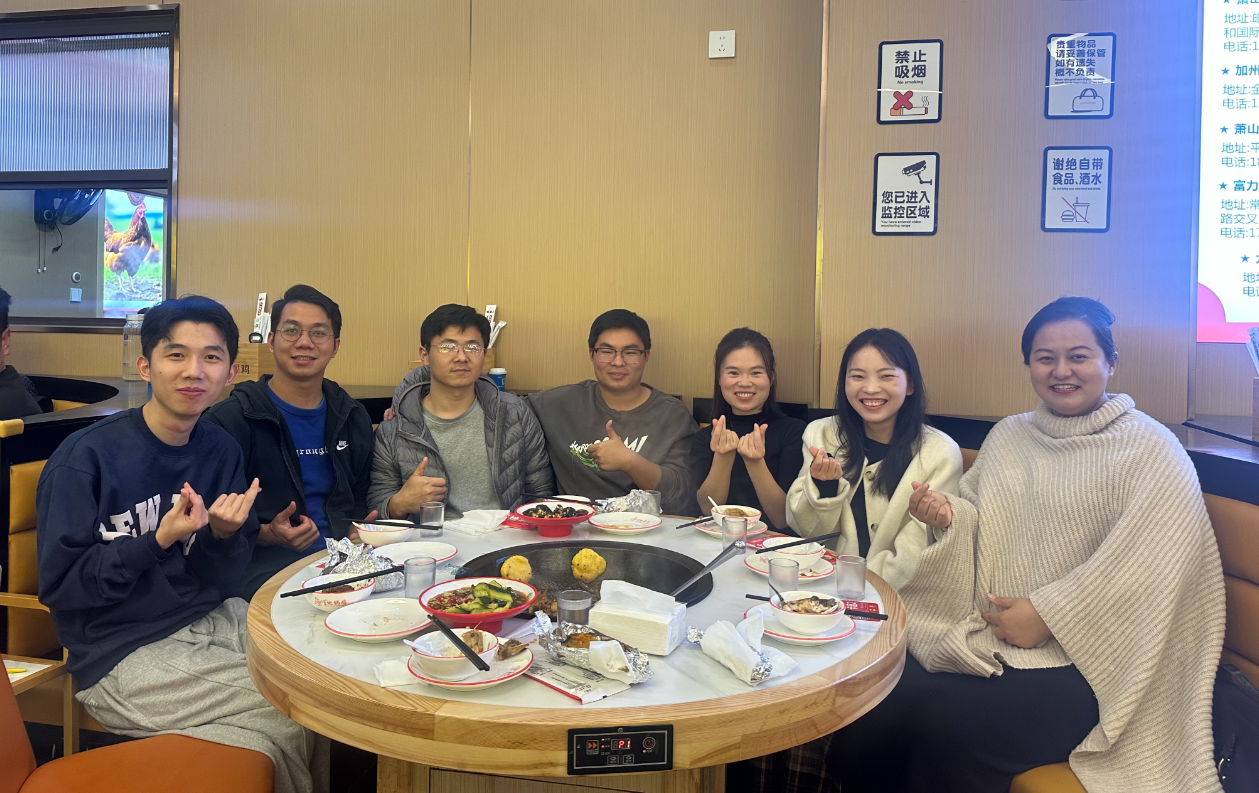 图片展示的是重庆破局圈友见面会的场景。七位圈友围坐在火锅桌旁，桌上摆放着火锅食材和餐具。圈友中有人比出“V”字手势，有人竖起大拇指，面带微笑，显得十分开心。背景墙上贴有禁止吸烟等标识，右侧有投影屏幕。此图与上文提到的“重庆破局圈友见面会”相呼应，直观呈现了线下聚会的欢乐氛围。