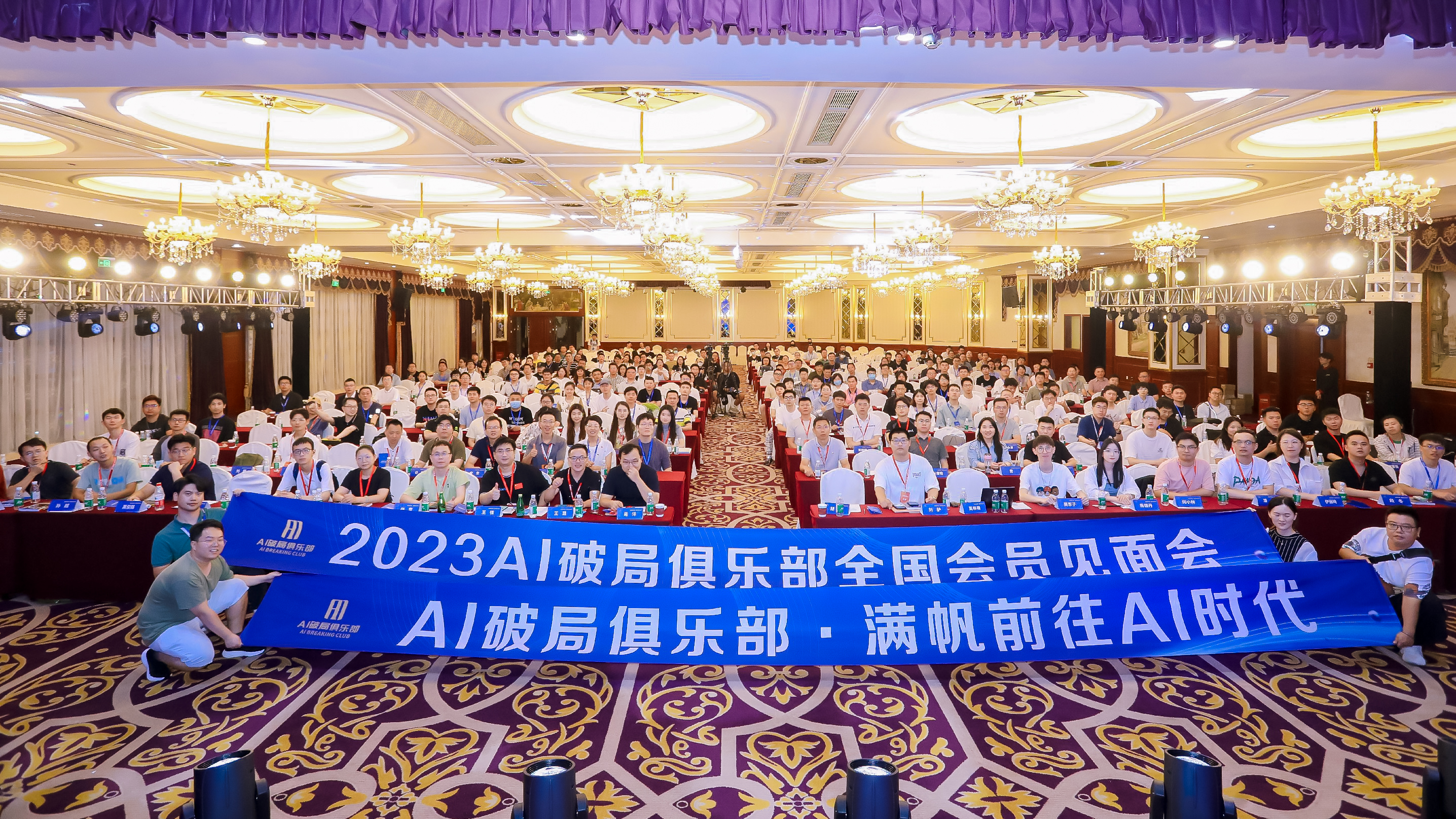 图片展示的是2023AI破局俱乐部全国会员见面会现场。会场内座无虚席，众多会员身着正装，气氛热烈。前方横幅上醒目地写着“2023AI破局俱乐部全国会员见面会 AI破局俱乐部·满帆前往AI时代”。会场布置华丽，天花板上悬挂着多个圆形吊灯，地面铺有花纹地毯。该图片与上文介绍的大会主题、嘉宾分享及线下见面会内容相呼应，直观呈现了大会盛况。