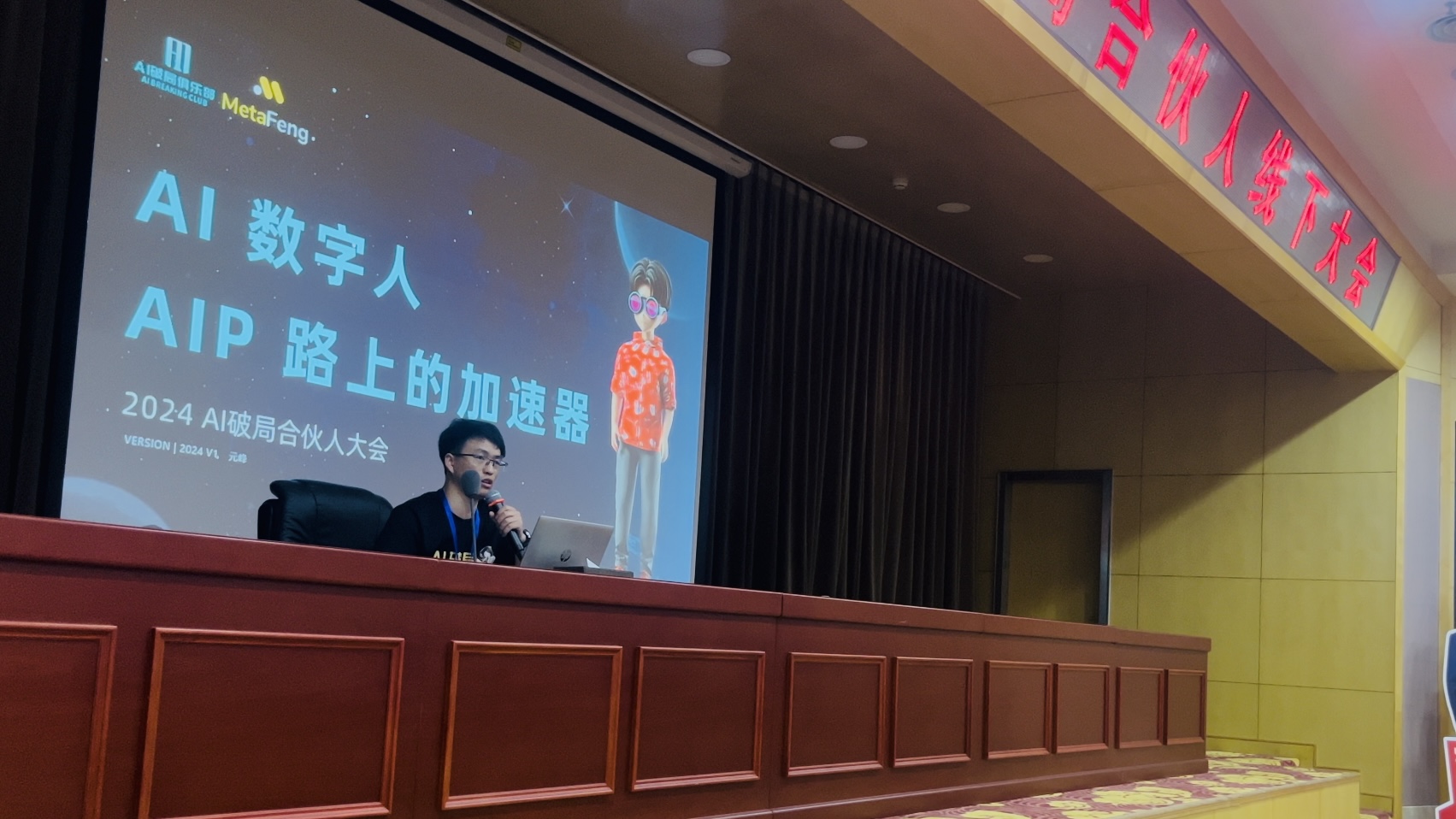 图片展示了2024 AI破局合伙人大会的现场场景。一位男士坐在讲台后发言，其身后的大屏幕上显示着 “AI数字人，AIP路上的加速器” 的标题，以及一个AI数字人的形象，屏幕左上角还有相关标识。背景中可以看到 “合伙人线下大会” 的红色字样。此图与文档内容紧密相关，直观呈现了文档中提及的AI破局合伙人大会现场，以及关于AI数字人的主题分享情况。
