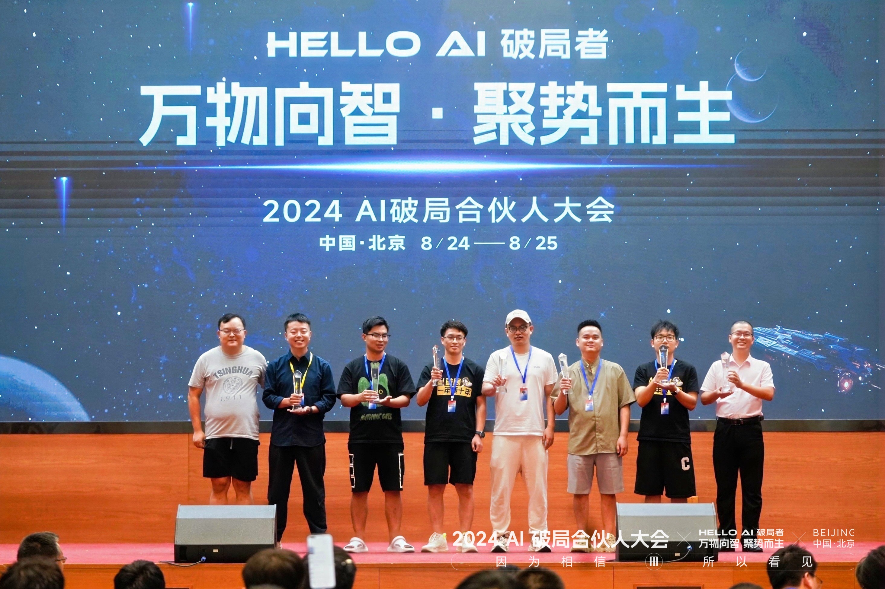 图片展示的是2024 AI破局合伙人大会现场。背景大屏幕上显示“HELLO AI 破局者 万物向智·聚势而生 2024 AI破局合伙人大会 中国·北京 8/24 - 8/25”。台上八位身着不同服装的男子手持奖杯或奖牌，其中一人戴白色帽子，一人穿白色T恤，一人穿浅色短袖，其余人着深色服装。台下观众席部分人头可见。此图与上下文提到的领奖内容相呼应，直观呈现了获奖场景。