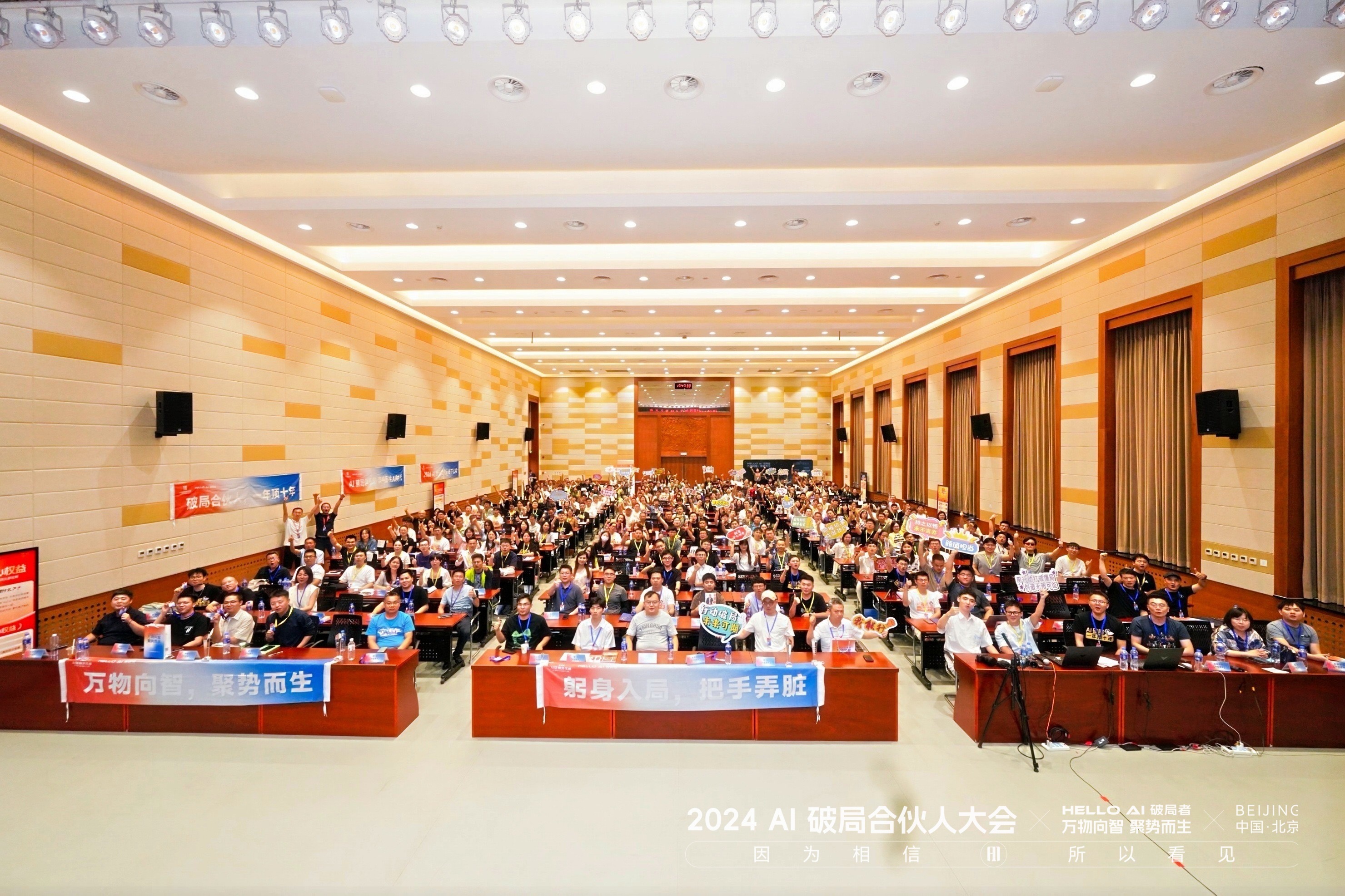 图片展示的是2024 AI破局合伙人大会现场。会场内座无虚席，观众席上坐满了人，部分人举着写有“万物向善，顺势而生”“躬身入局，携手弄脏”等标语的牌子。会场前方有红色横幅，上面写着“2024 AI破局合伙人大会”及“因为相信，所以看见”。背景墙上有“HELLO AI”“BEIJING”字样。此图与文档中对大会的介绍相契合，直观呈现了大会盛况。