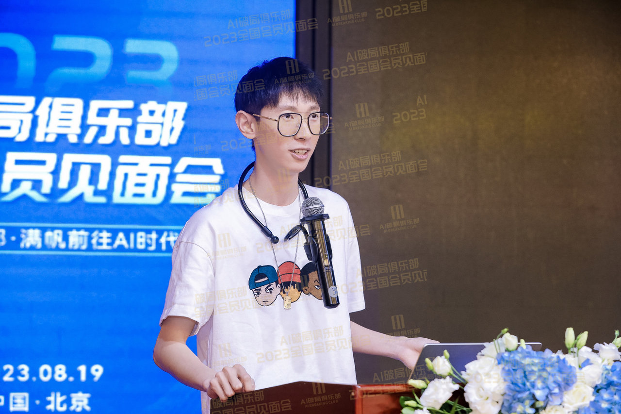 图片展示的是2023年8月19日在北京举办的AI领航俱乐部全国会员见面会现场。画面中一位男士站在讲台前，手持麦克风，身着白色T恤，T恤上有卡通人物图案。背景为蓝色屏幕，上面有“2023 AI领航俱乐部全国会员见面会”等字样。讲台前方摆放着一束花。该图片与文档中介绍的会议内容相关，直观呈现了会议现场情况。