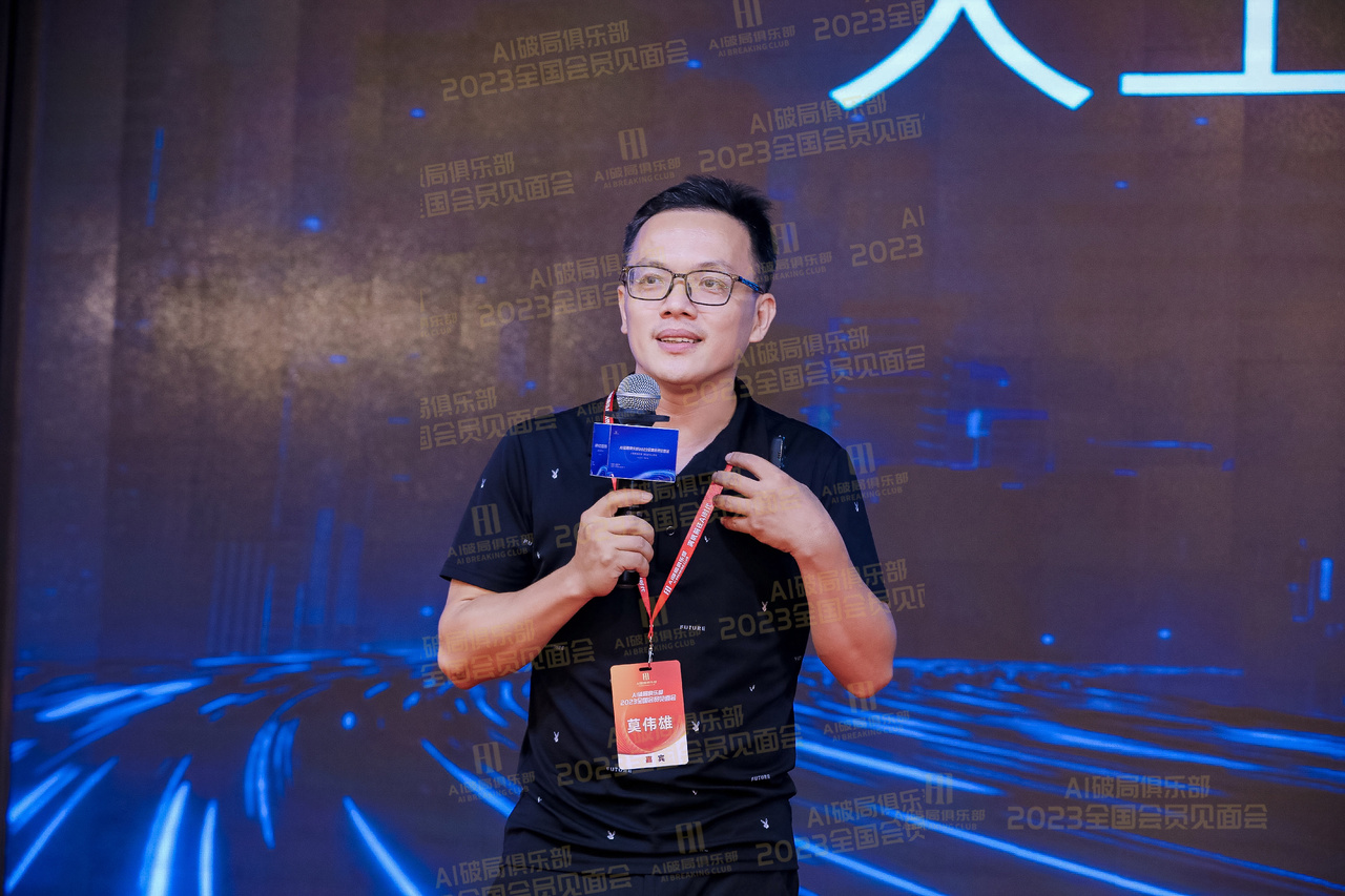 图片展示的是2023年AI破局俱乐部全国会员见面会现场。画面中一位男士手持麦克风，身着黑色T恤，佩戴红色证件，背景为深色带有蓝色光效的舞台，上方有“AI破局俱乐部 2023全国会员见面会”字样。该图片位于文档中“莫总:企业如何人工智能”部分之前，可能是作为该部分内容的开场或结尾场景展示，直观呈现了活动氛围。