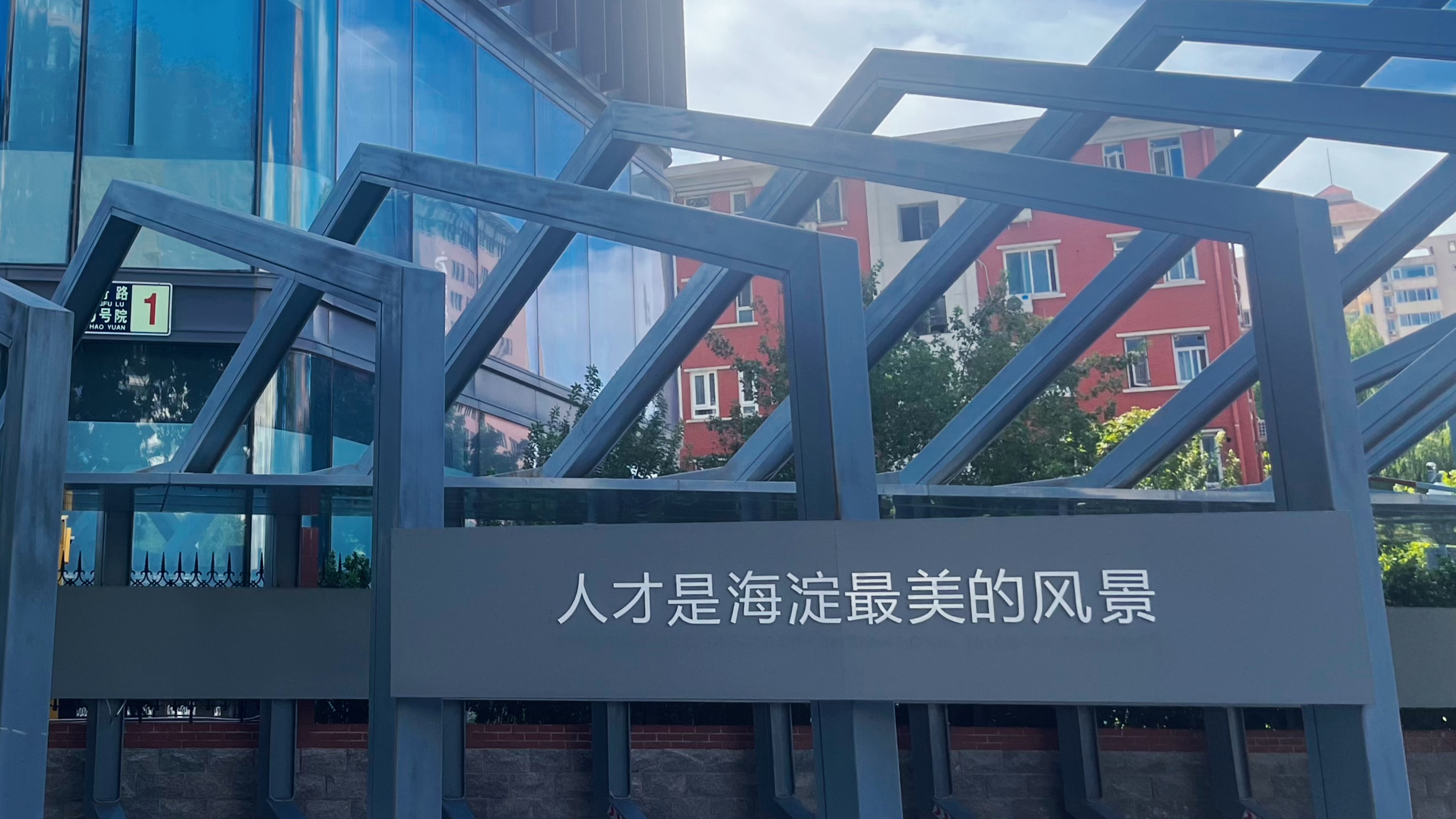 图片展示的是北京海淀区的一处建筑入口，入口上方有“1”字样的标识。入口处的金属框架结构上，醒目地写着“人才是海淀最美的风景”字样。这张图片与上下文紧密相关，上下文提到“人才是海淀最美的风景”是北京这座城市的最好诠释，强调了人才在海淀发展中的重要性，图片直观呈现了这一理念，与文档中对人才重要性的阐述相呼应。