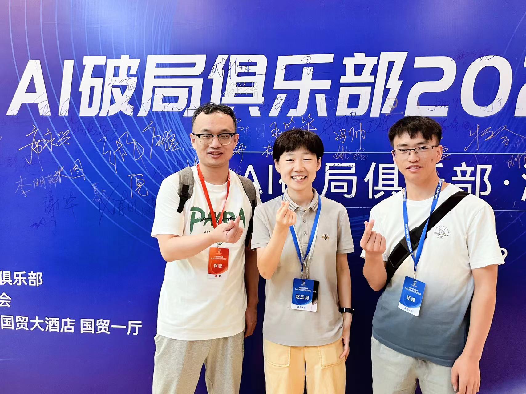 图片展示了三位参加AI破局俱乐部2023北京之旅的人员。背景为蓝色，写有“AI破局俱乐部2023”等字样，还标注了会议地点“国贸大酒店 国贸一厅”。三人中，中间的女性面带微笑，比出“V”字手势；两侧的男性则做出类似手势。他们胸前佩戴着不同颜色的证件，背景上还有多位参会人员的名字。此图与上文提到的AI破局俱乐部北京之旅相呼应，记录了活动参与者合影的场景。