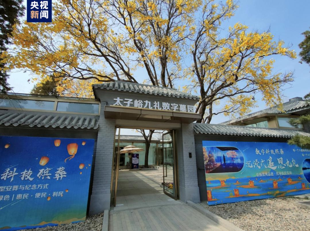 图片展示的是北京太子峪九礼数字墓园的入口。入口上方有“太子峪九礼数字墓园”的字样,两侧墙上分别有宣传海报,左侧写着“科技殡葬”等内容,右侧有“数字科技殡葬”等字样。墓园入口处有树木,树叶呈现出金黄色。该图片与上下文的关系是,作为北京数字墓园的实景呈现,直观展现了文中所提及的中国殡葬行业数字化革命中数字墓园的场景,为介绍北京数字墓位等相关内容提供了视觉参照。