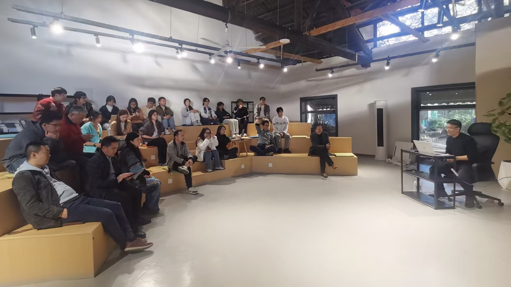 图片展示了一场N8N专题培训的场景。培训地点在一个室内空间,天花板上有排列整齐的射灯。左侧有几位坐在黄色沙发上的学员,他们或专注听讲,或低头记录。右侧有一位坐在黑色办公椅上的讲师,他手持文件,正在讲解。背景中还有几扇窗户,窗外景色隐约可见。此图与文档中“昨天搞了一场N8N专题培训”的内容相契合,直观呈现了培训现场情况。