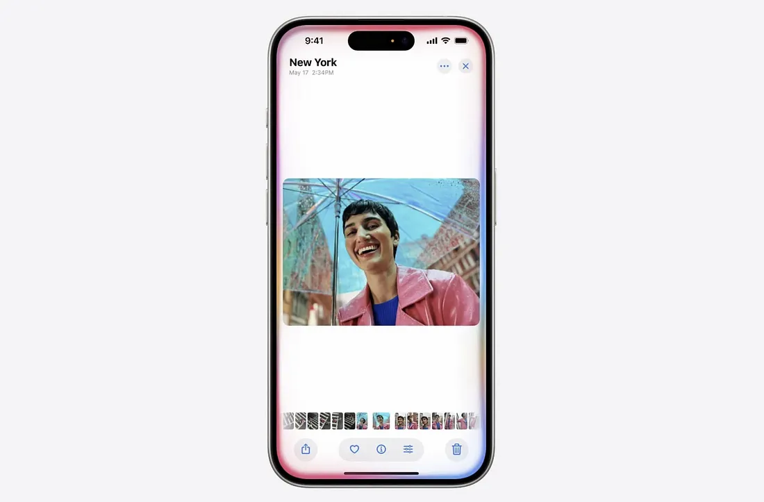 图片展示了一部iPhone屏幕,显示时间为9:41,地点为New York。屏幕上有一张照片,照片中一位穿着粉色外套、蓝色内搭的人在雨中笑得很开心,背景是城市街景。屏幕下方有多个小图标,包括相机、表情符号、画笔等。该图片与上下文紧密相关,直观呈现了新的Siri能够自己操作,通过Ferret-UI视觉语言模型看懂iOS屏幕上的图标、小部件和文字,还能搞明白它们之间的关系和作用这一功能。